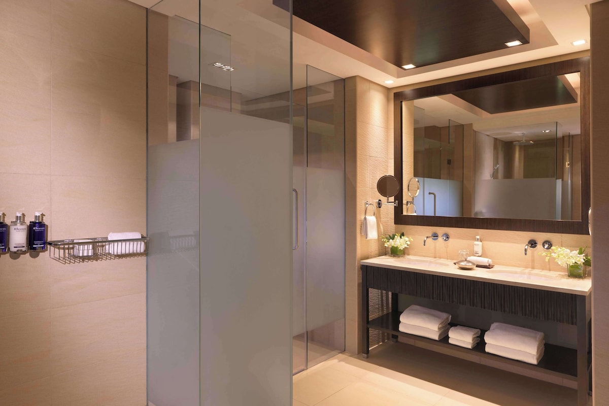 Een moderne badkamer met een glazen douchecabine, een grote spiegel en een wastafelmeubel met een handdoekhouder.