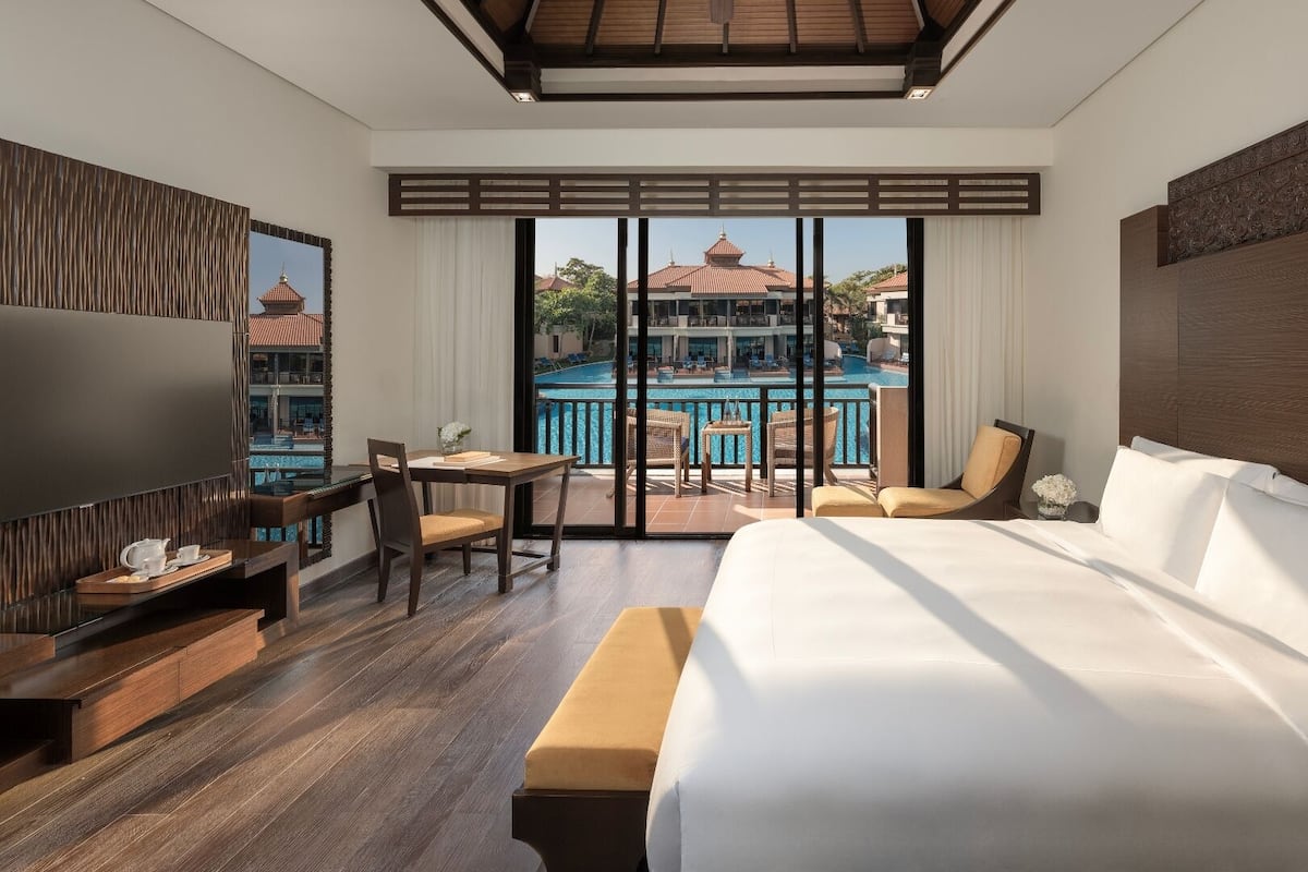 Hotelkamer met een groot bed, een bureau met stoel, een televisie en een balkon met uitzicht op het zwembad.