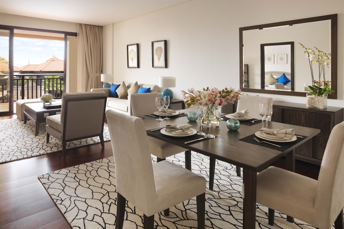 Een eetgedeelte met een tafel voor vier personen, een bank en een balkon met uitzicht op gebouwen.