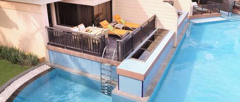 A rooftop pool area with a glass balustrade, lounge chairs, and a small table.