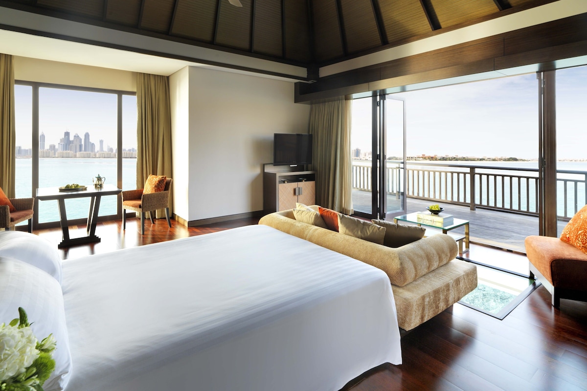 Een hotelkamer met een groot bed, een bank, een televisie en een balkon met uitzicht over de stad.
