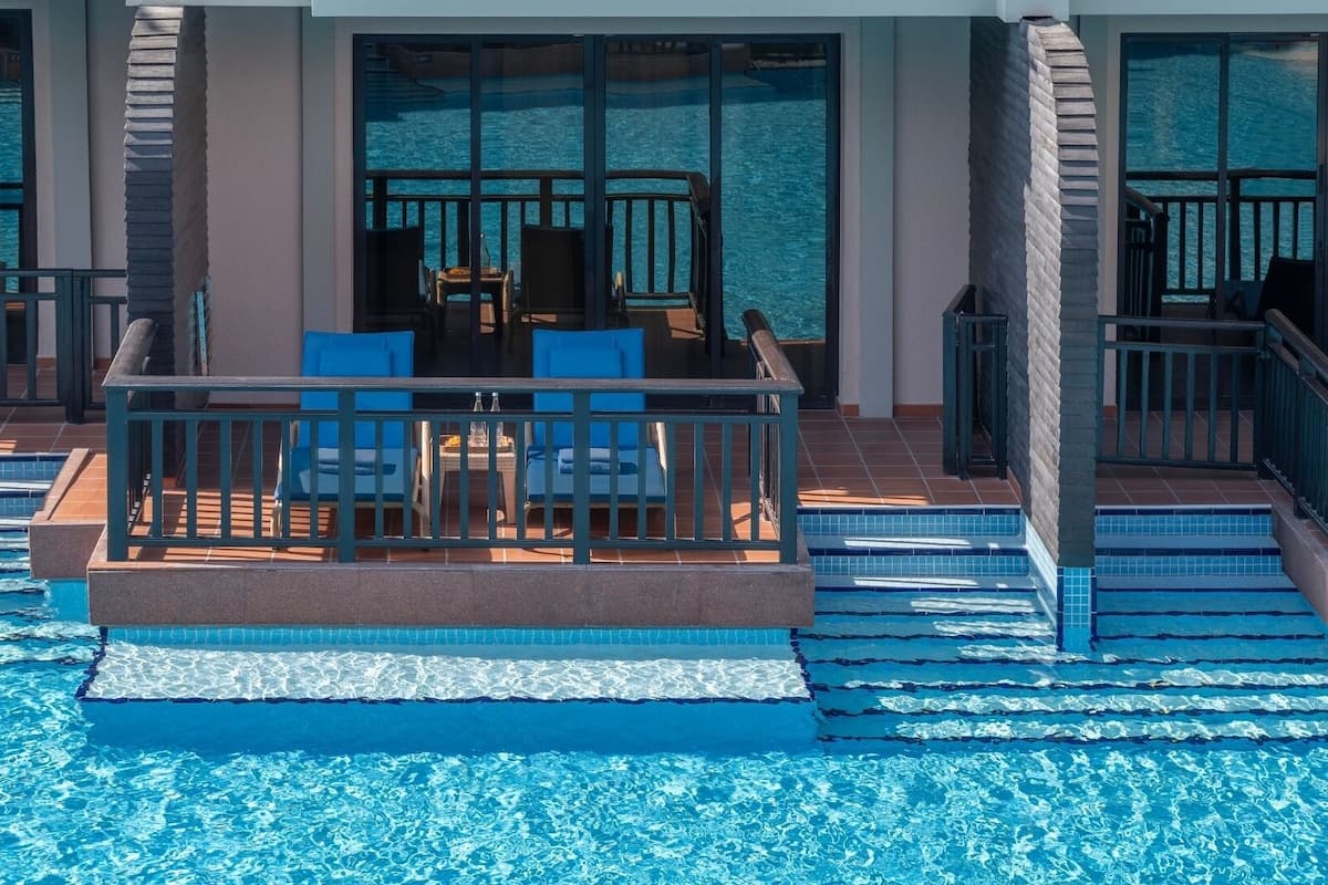Een zwembadterras met een tafel en stoelen, een zwembad met helderblauw water en uitzicht op de oceaan door grote ramen.