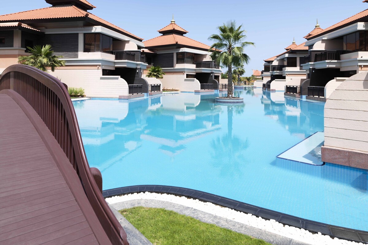 Een resort met een groot zwembad, meerdere gebouwen met rode pannendaken en palmbomen.