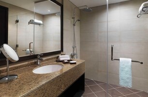 A modern bathroom with a granite countertop, a large mirror, a shower with a handheld showerhead, and a towel rack.