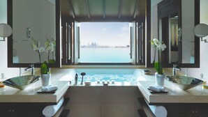 Ein Badezimmer mit zwei Waschbecken, einem großen Spiegel und Blick auf eine Stadtlandschaft durch geöffnete Fensterläden.
