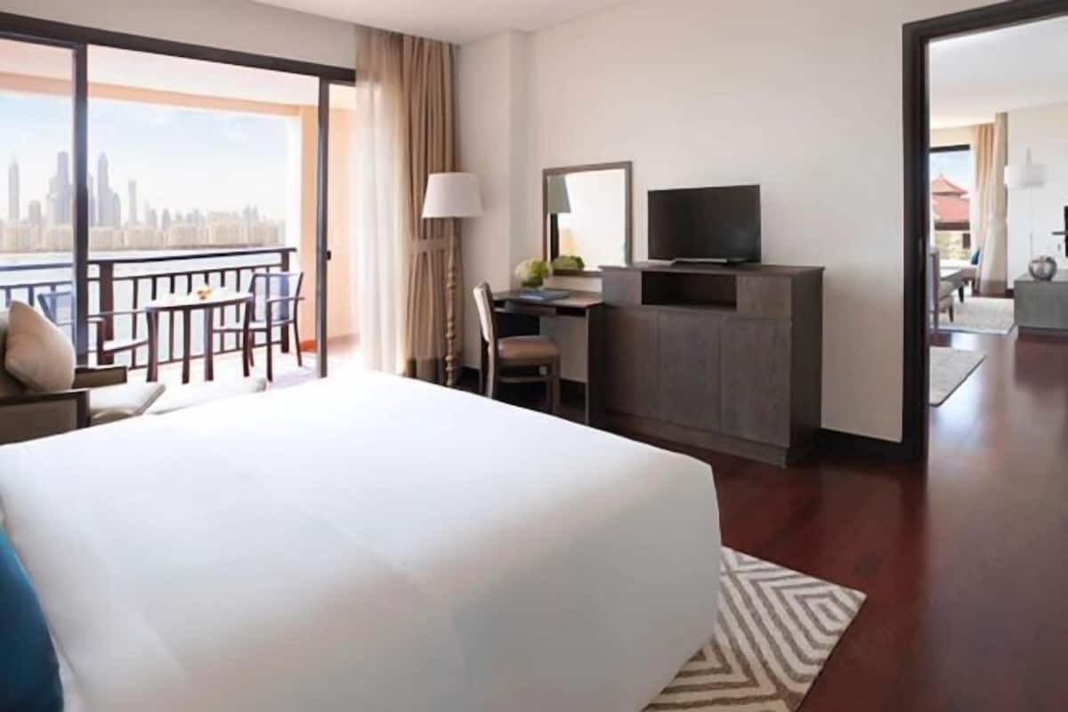 Habitación de hotel con cama, escritorio, televisión y balcón con vista a la ciudad.