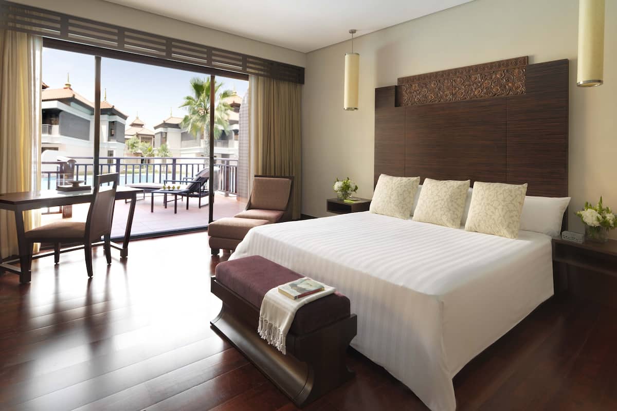 Ruime hotelkamer met een groot bed, een zithoek met een tafel en stoelen, en een balkon met uitzicht op het resort.