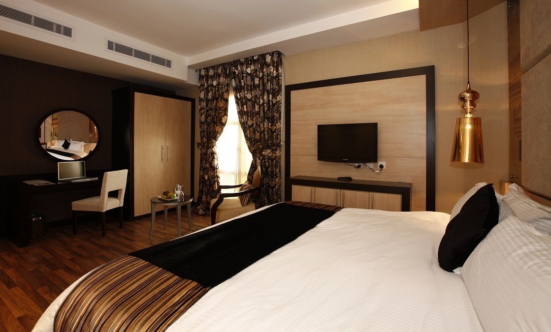 Quarto de hotel com uma cama grande, uma escrivaninha com cadeira, uma televisão e um espelho.