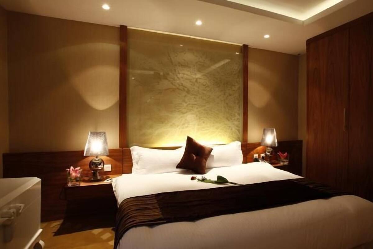 Una habitación de hotel con una cama grande, dos mesitas de noche con lámparas, un armario de madera y una obra de arte colgada en la pared.