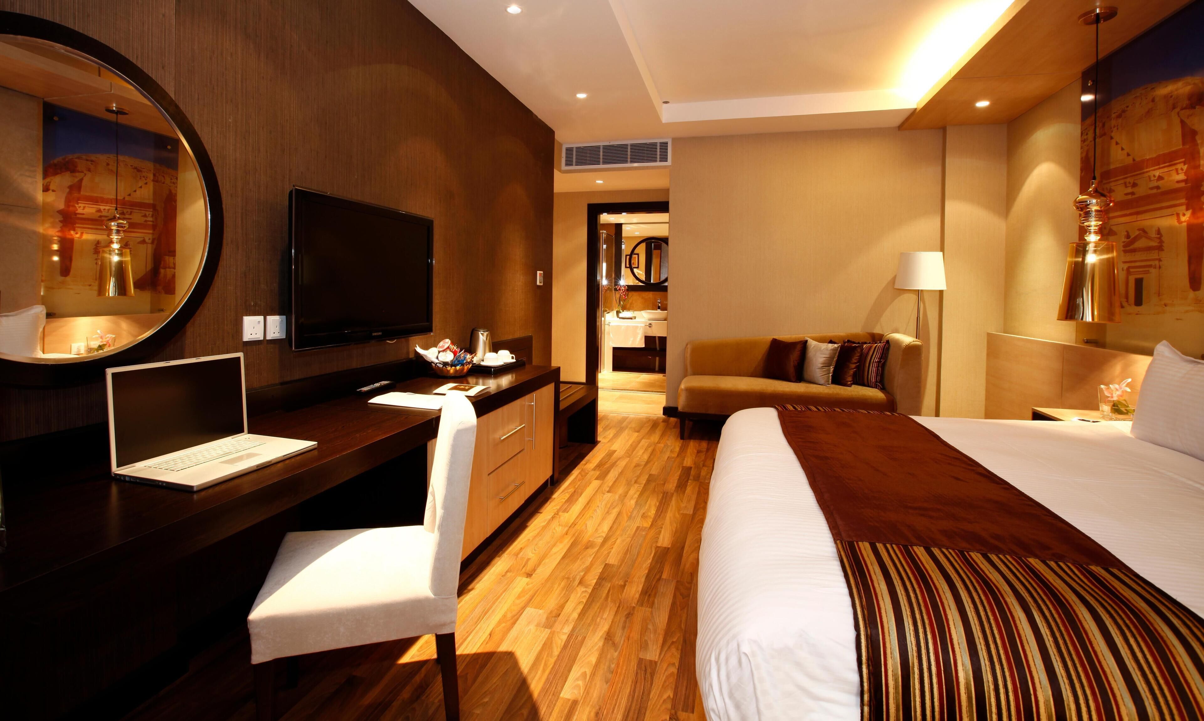 A hotel room with a bed, a desk with a laptop, a television, and a mirror.