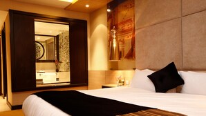 A hotel room with a large bed, a nightstand, a mirror, and a wall-mounted lamp. - Grand Plaza Hotel - Takhasosi Riyadh (Riyadh)