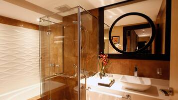 A modern bathroom with a glass-enclosed shower, a white sink with a vase of flowers, and a large mirror with a circular frame.