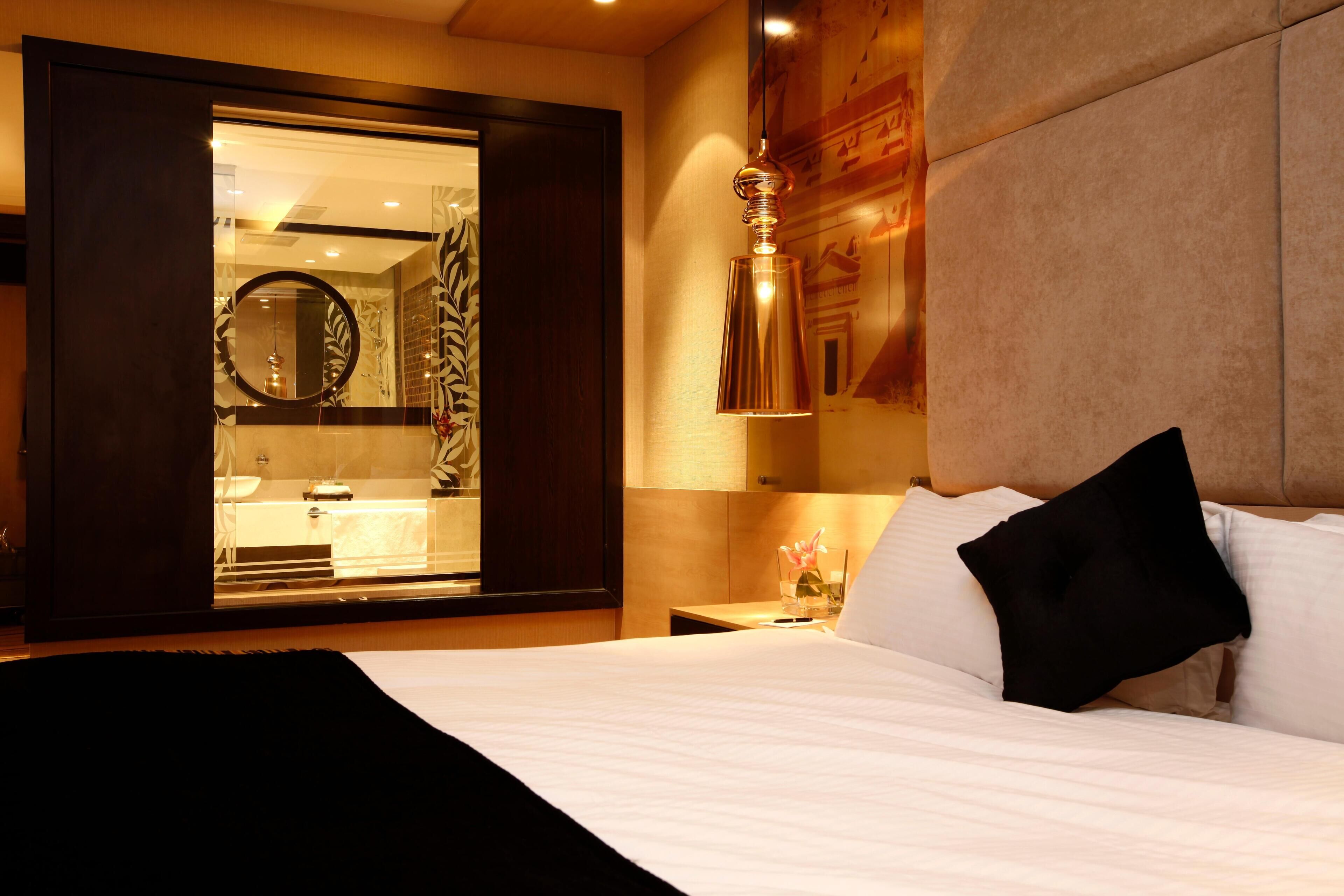 Una habitación de hotel con cama, mesita de noche, espejo y un panel decorativo en la pared.