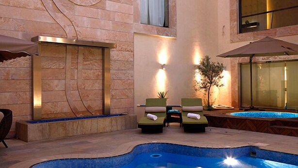 A swimming pool with two lounge chairs and a small table, surrounded by stone walls with decorative carvings. - Grand Plaza Hotel - Takhasosi Riyadh (Riyadh)