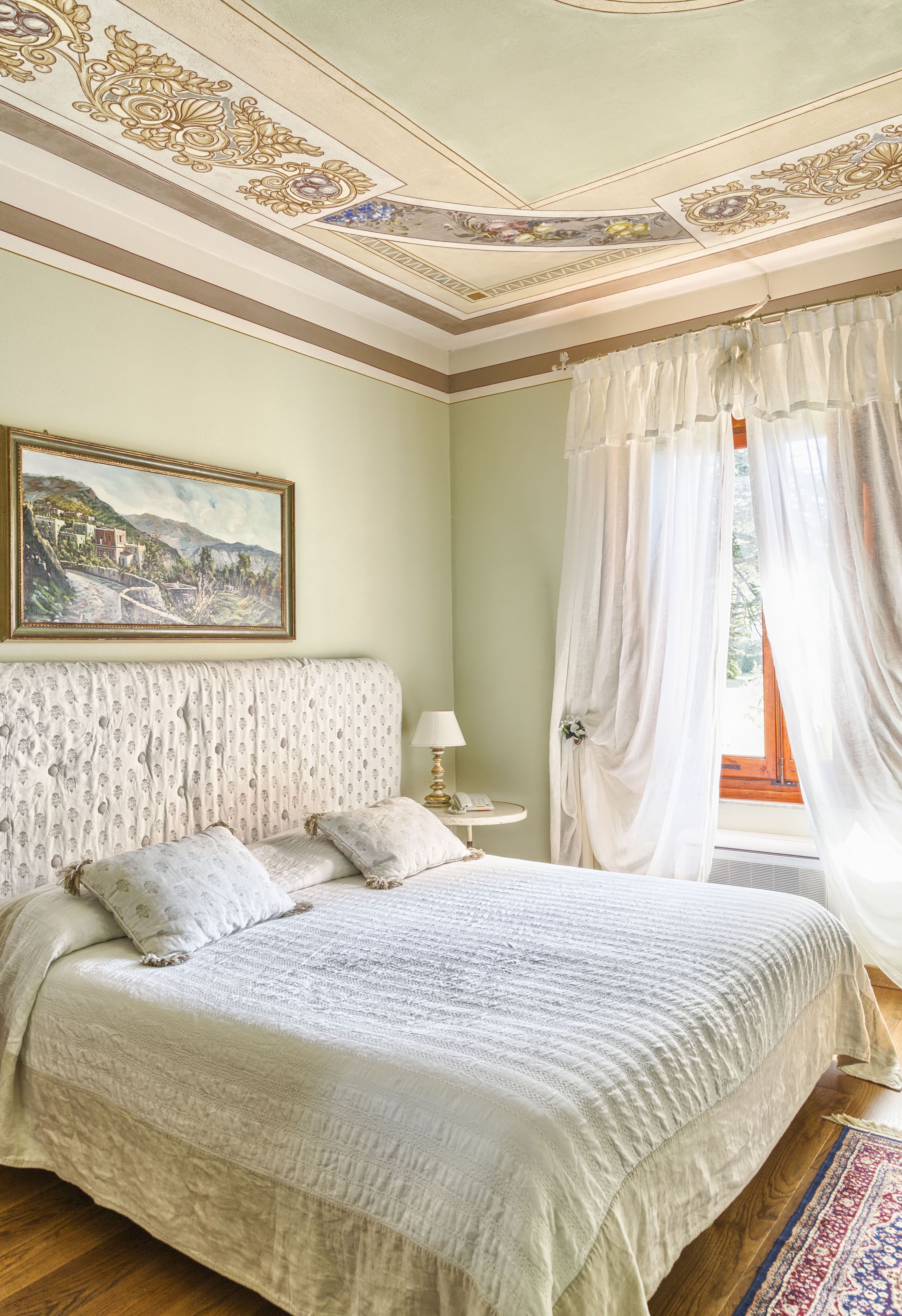 A bedroom with a large bed, a nightstand, a lamp, and a painting on the wall.