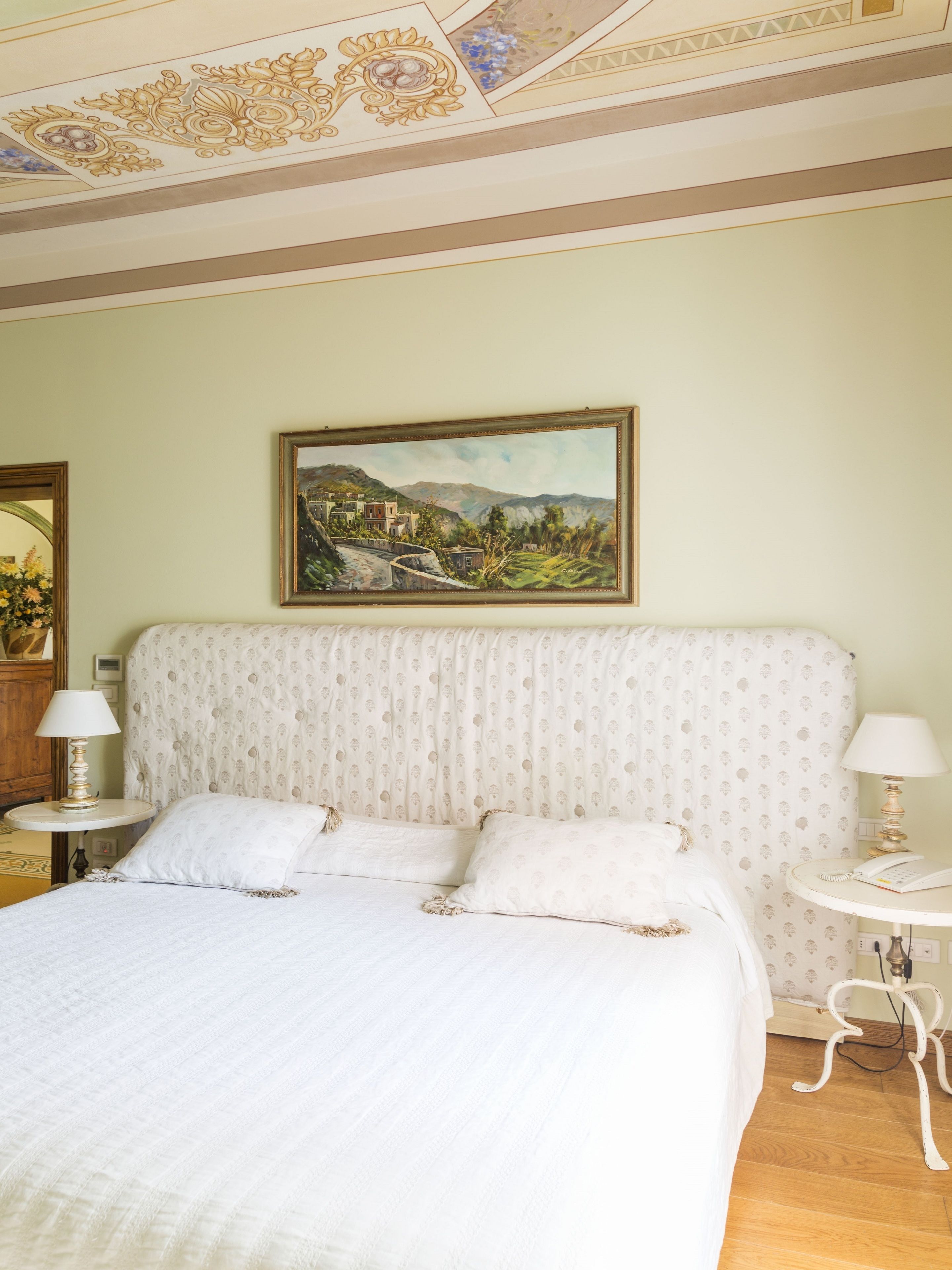 Une chambre à coucher bien rangée, avec un lit, deux tables de chevet, un tableau au mur et une tête de lit à motifs.