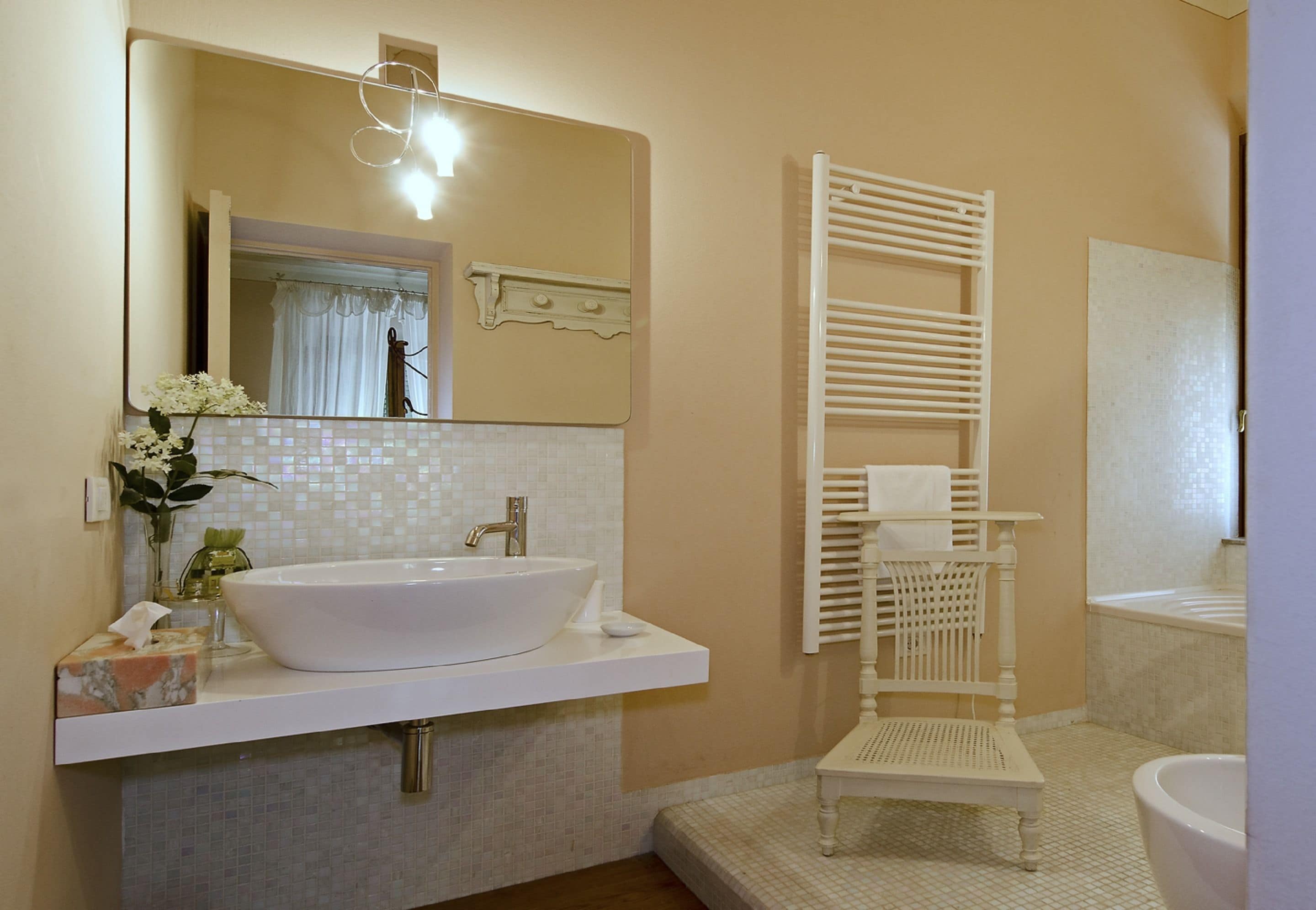 A bathroom with a large white sink, a mirror, a towel rack, and a small white chair.