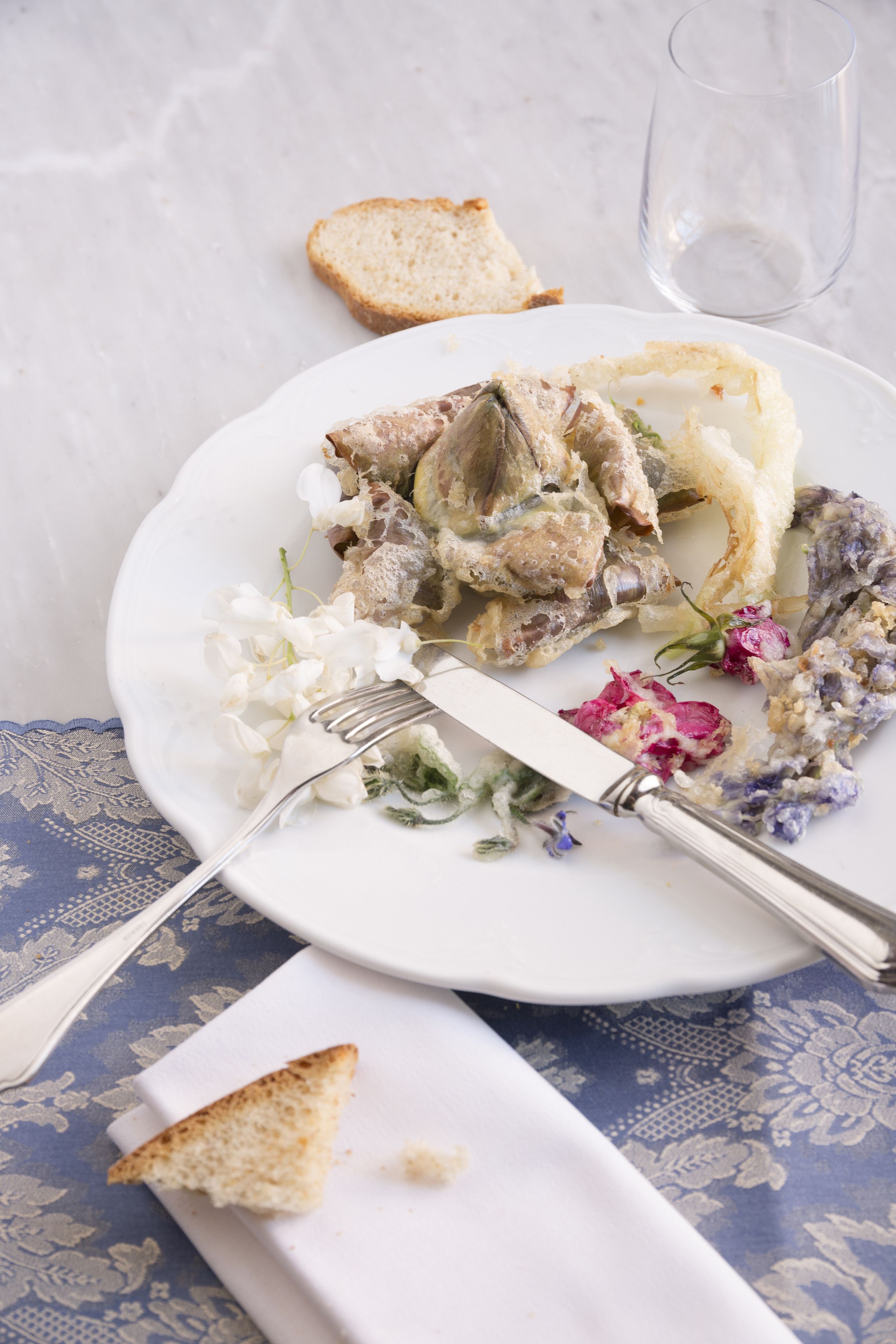 A plate with food remnants, a fork, and a glass on a table with a patterned tablecloth.