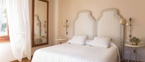 A bedroom with a large bed, a bedside table, a nightstand, a mirror, and a window with curtains.