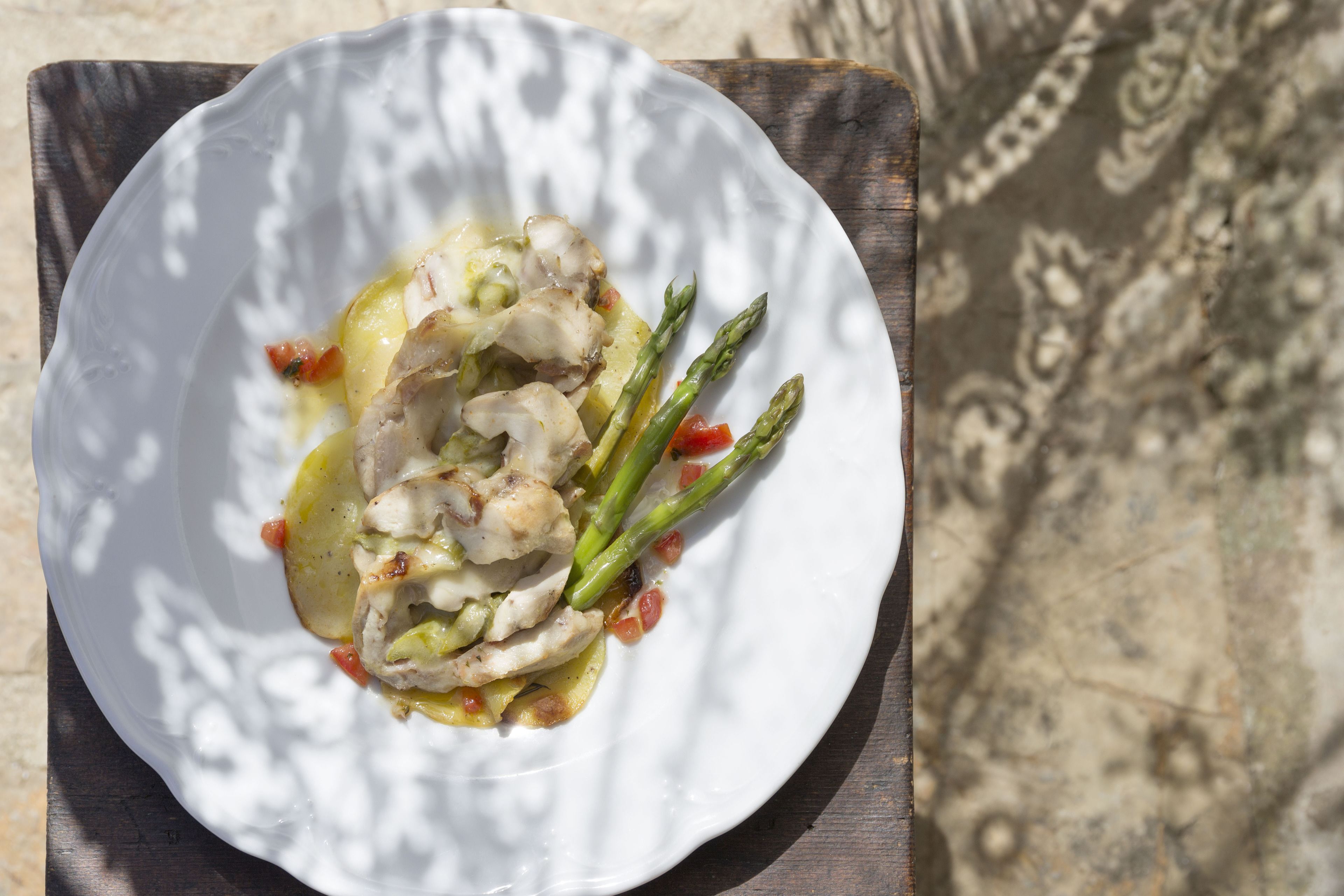 Een wit bord met gegrilde kip, asperges en saus op een houten tafel.