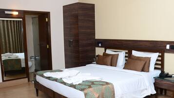 A hotel room with a large bed, a wooden wardrobe, a bedside table with a phone, and a ceiling fan.