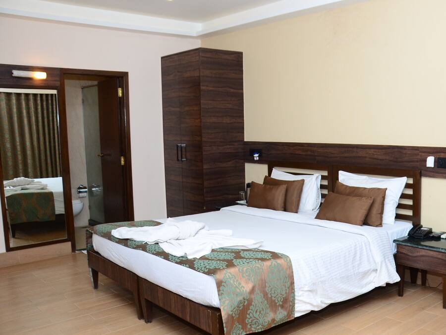 A hotel room with a large bed, a wooden wardrobe, a bedside table with a phone, and a ceiling fan.