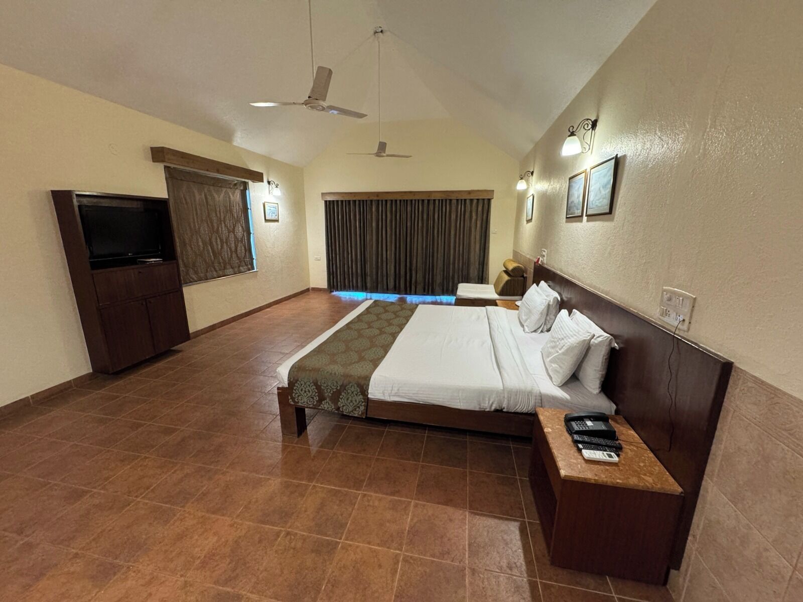 A hotel room with a large bed, a TV, a desk with a telephone, and a ceiling fan.
