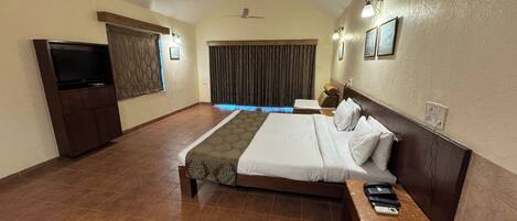 Habitación de hotel con una cama grande, televisión, escritorio con teléfono y ventilador de techo.