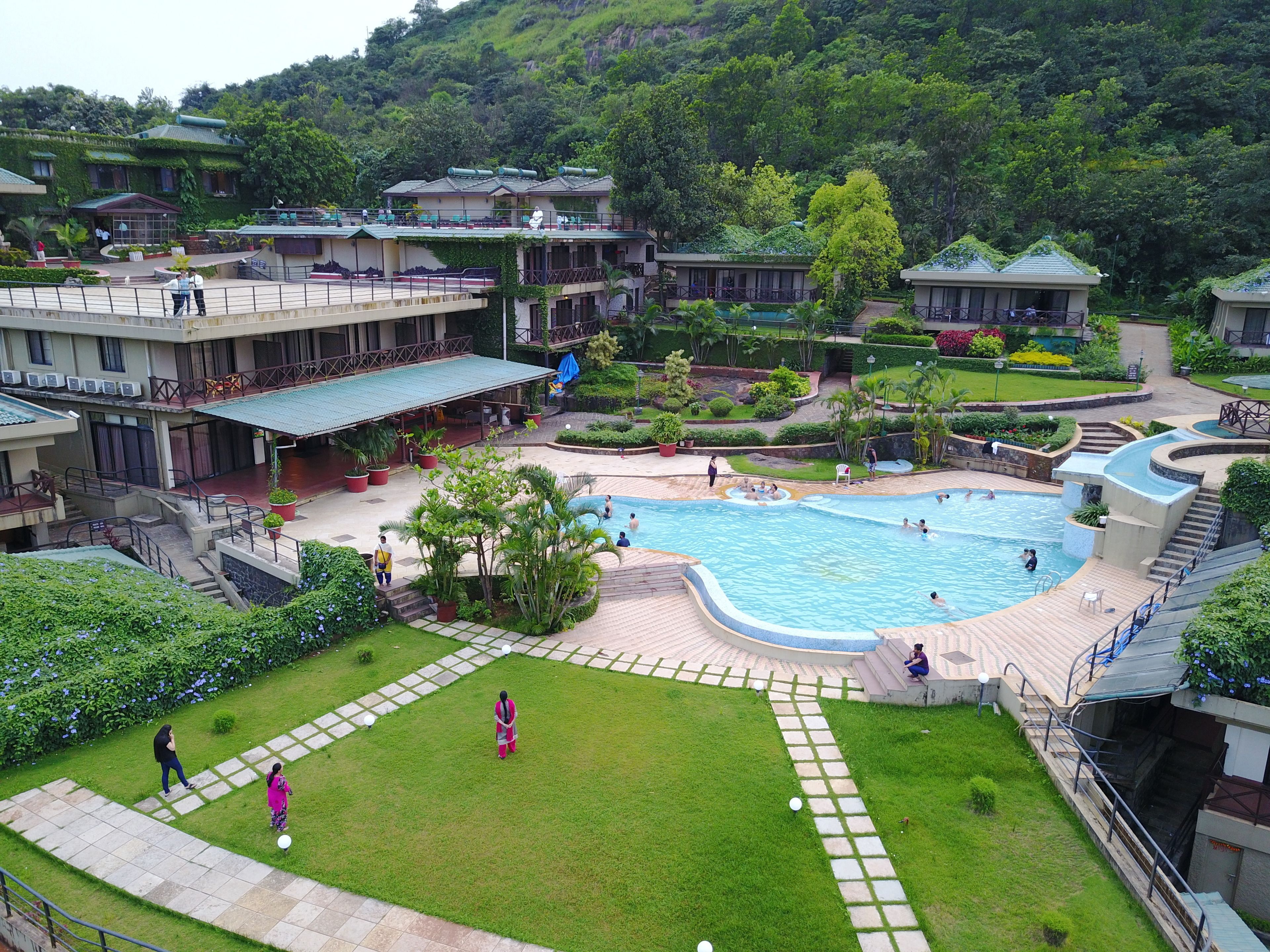 A hotel with a swimming pool, green lawns, and a mountainous backdrop.