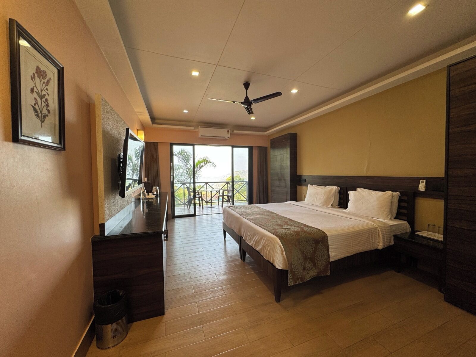 A hotel room with a large bed, a desk, a ceiling fan, and a balcony with outdoor seating.