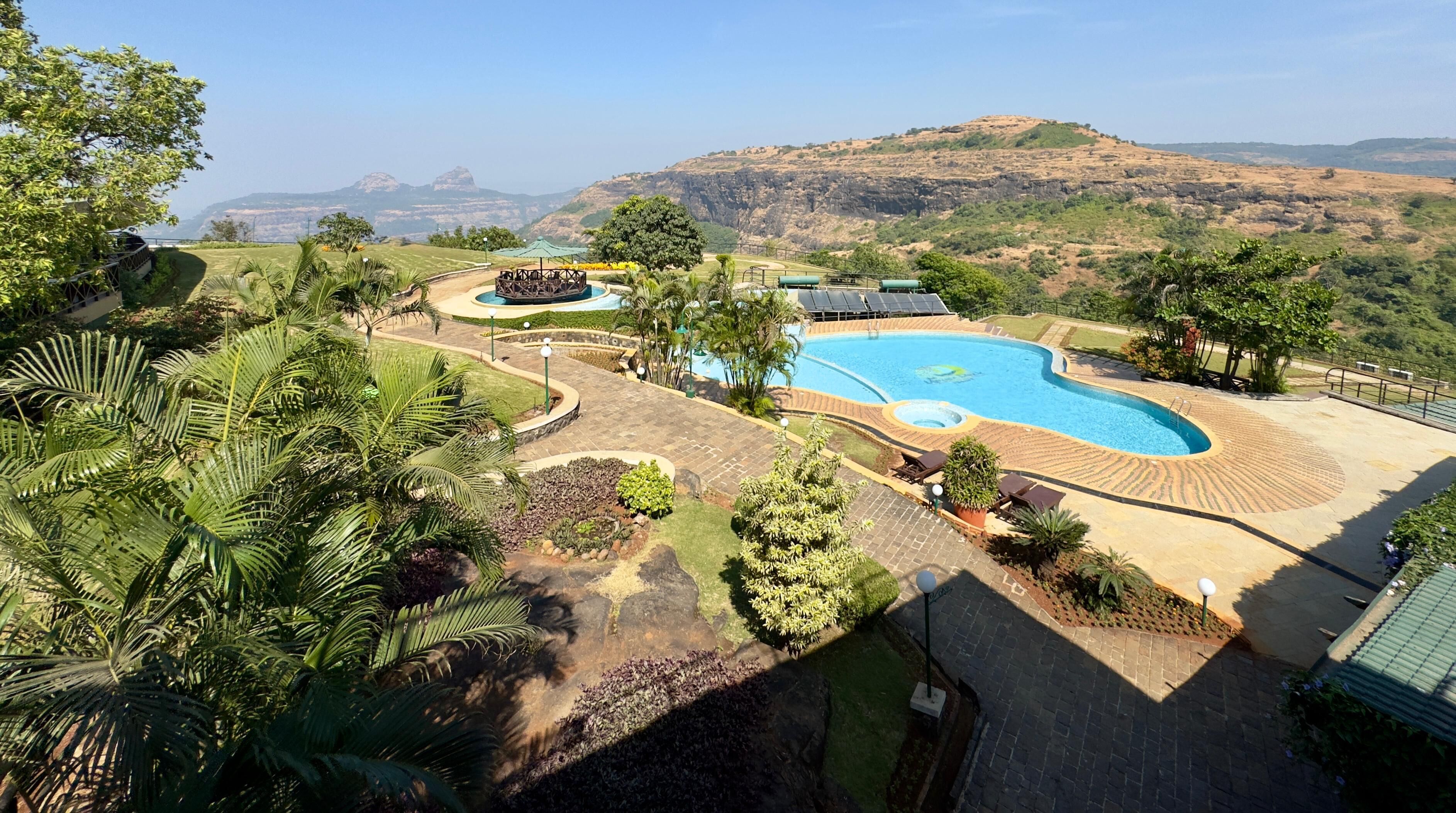 Un resort con una amplia piscina, palmeras y vistas a colinas distantes.