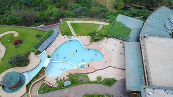 Une vue aérienne d’un hôtel doté d’une grande piscine, de jardins aménagés et d’un espace couvert avec des sièges.