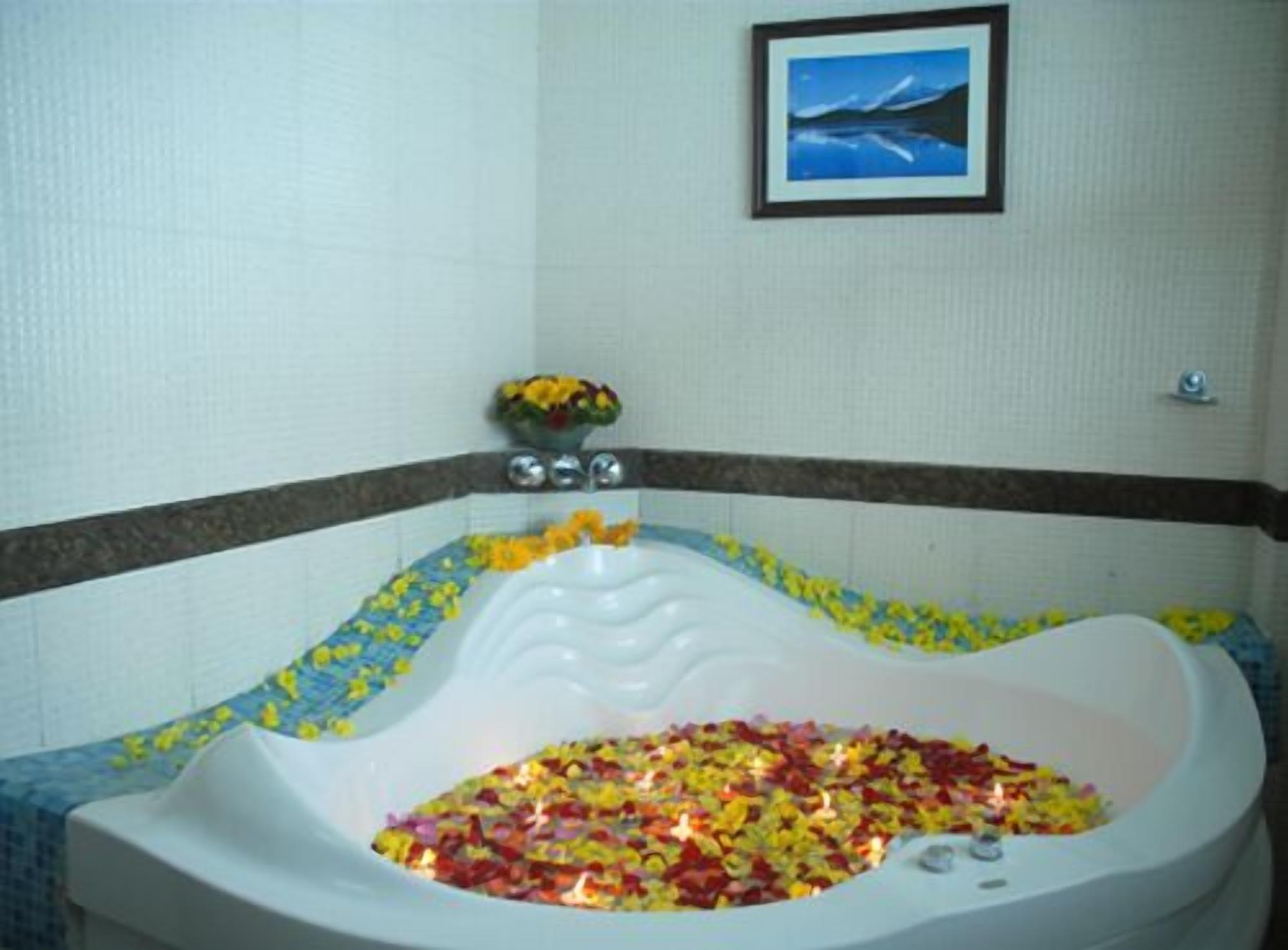 A bathtub filled with colorful bath bombs and flowers, a framed picture on the wall, and a small vase with flowers on the side.