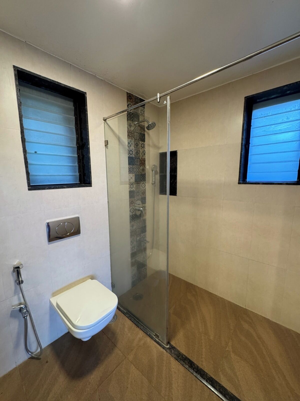 Un baño moderno con ducha envuelta en vidrio, inodoro y ventana.