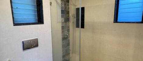 Un baño moderno con ducha envuelta en vidrio, inodoro y ventana.