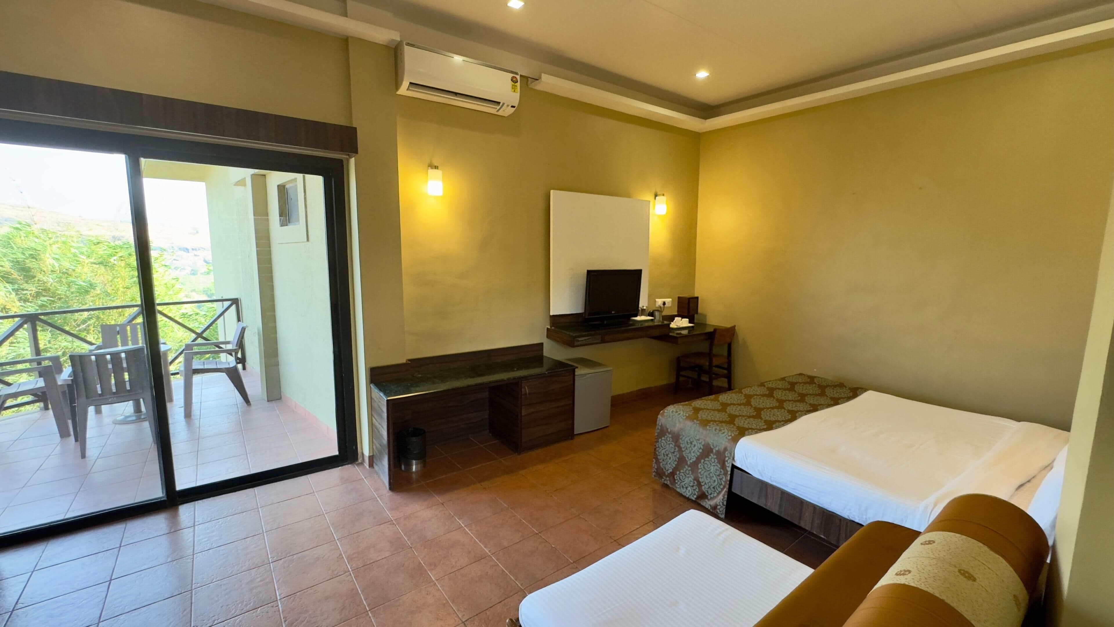 A hotel room with a balcony, a desk with a television, a bed, and a sofa.