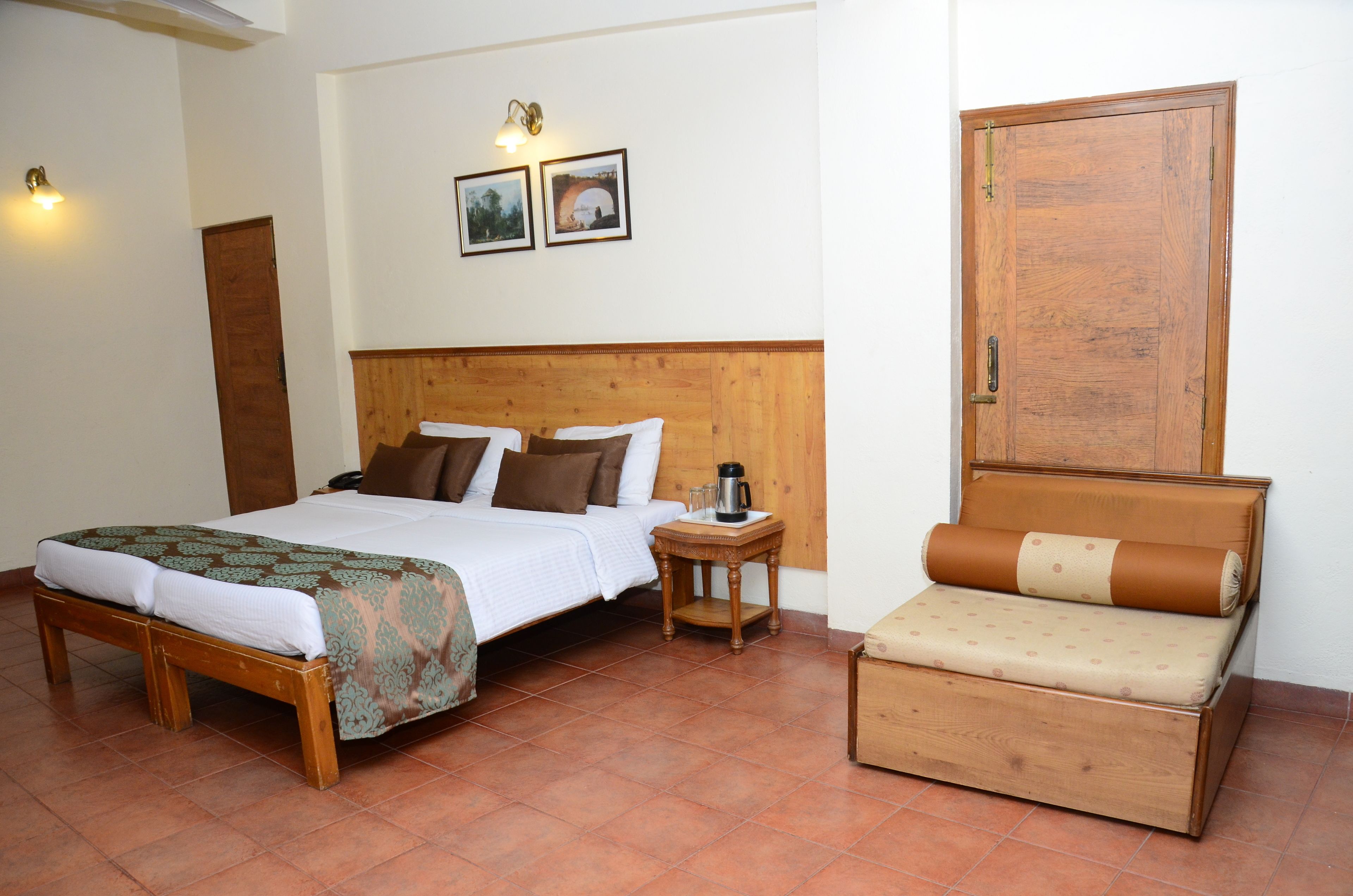 A bedroom with a wooden bed, a bedside table with a lamp, a wooden cabinet, and a small wooden bench.