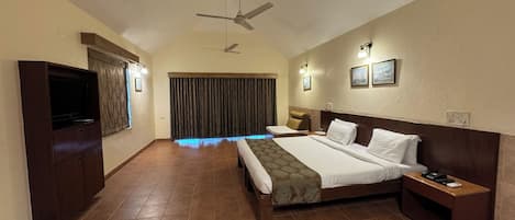 A hotel room with a large bed, a TV, a ceiling fan, and a window with curtains.
