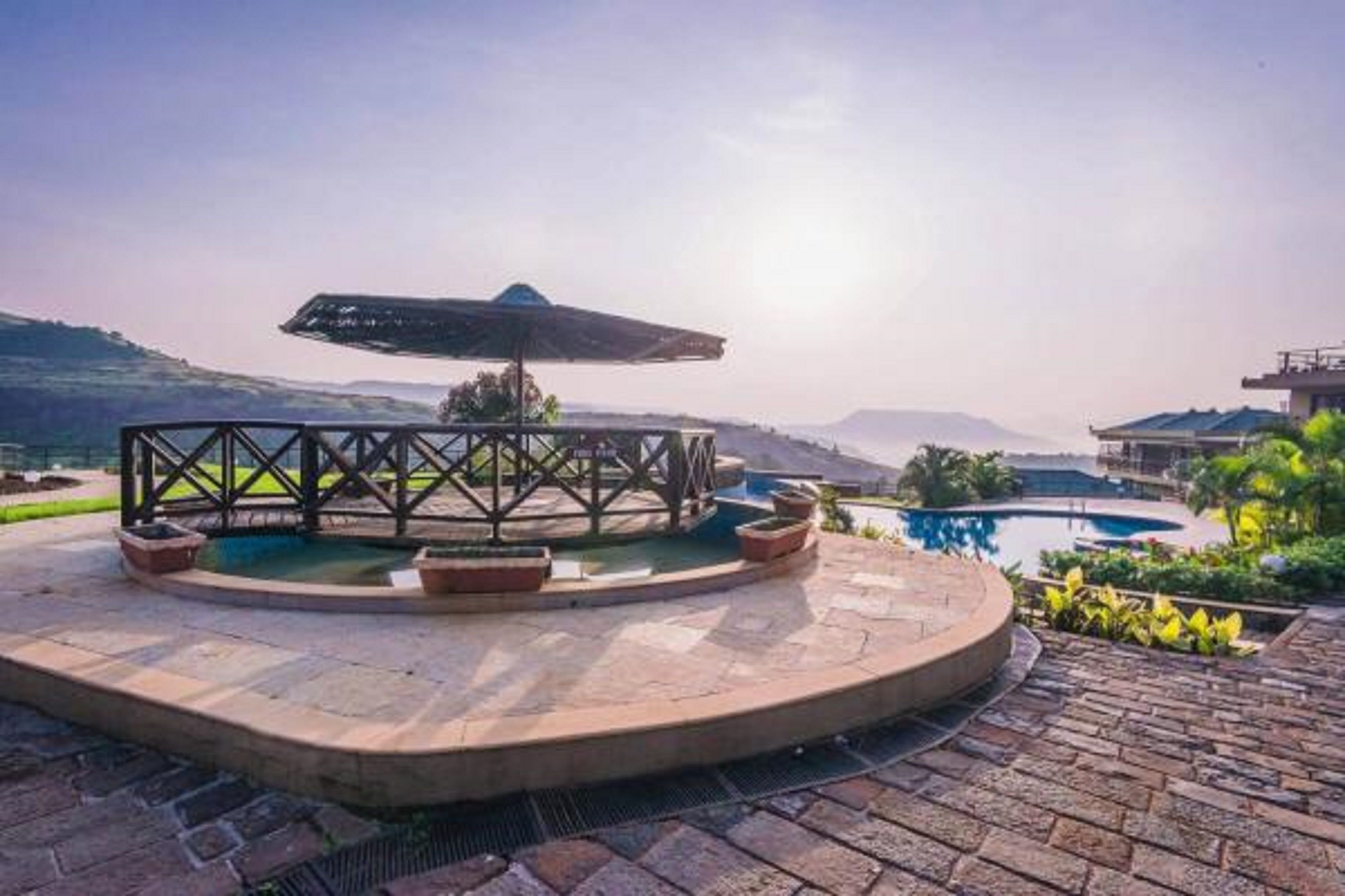 A circular outdoor seating area with a pool, surrounded by a stone patio and a metal fence.