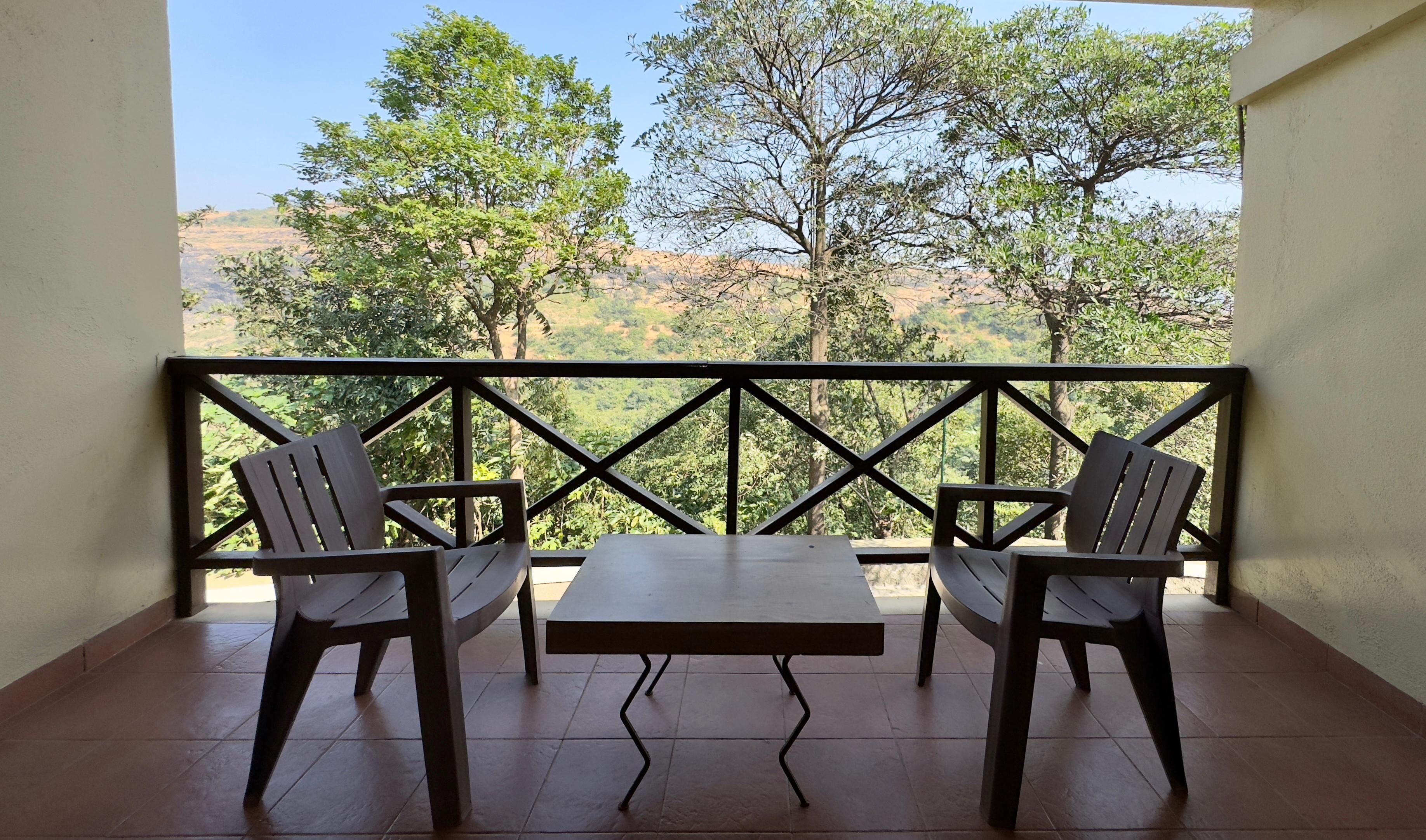 Un balcón con dos sillas y una mesa, con vistas a un paisaje montañoso con árboles.