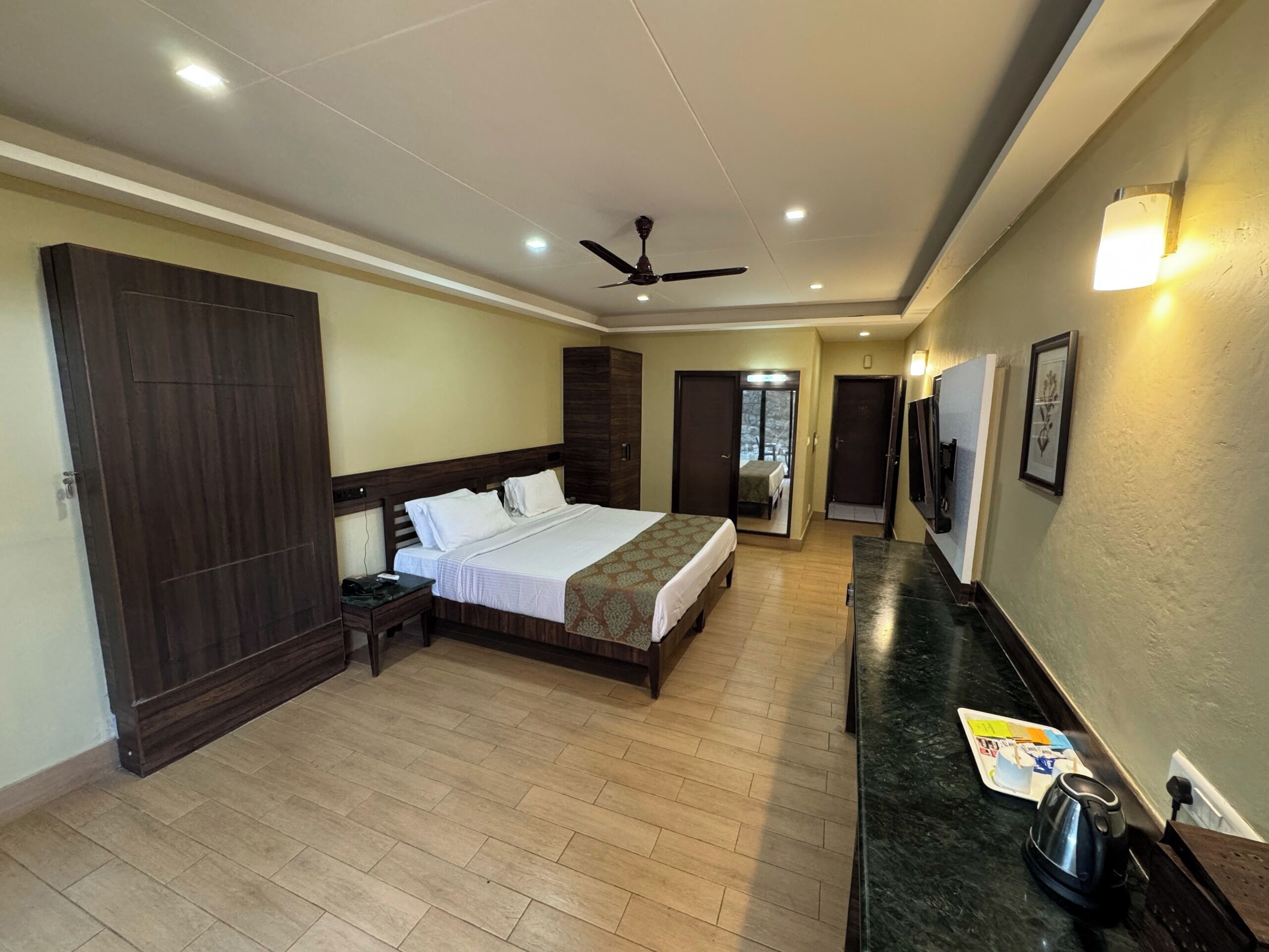 A hotel room with a bed, a desk, a wardrobe, a ceiling fan, and a bathroom door.