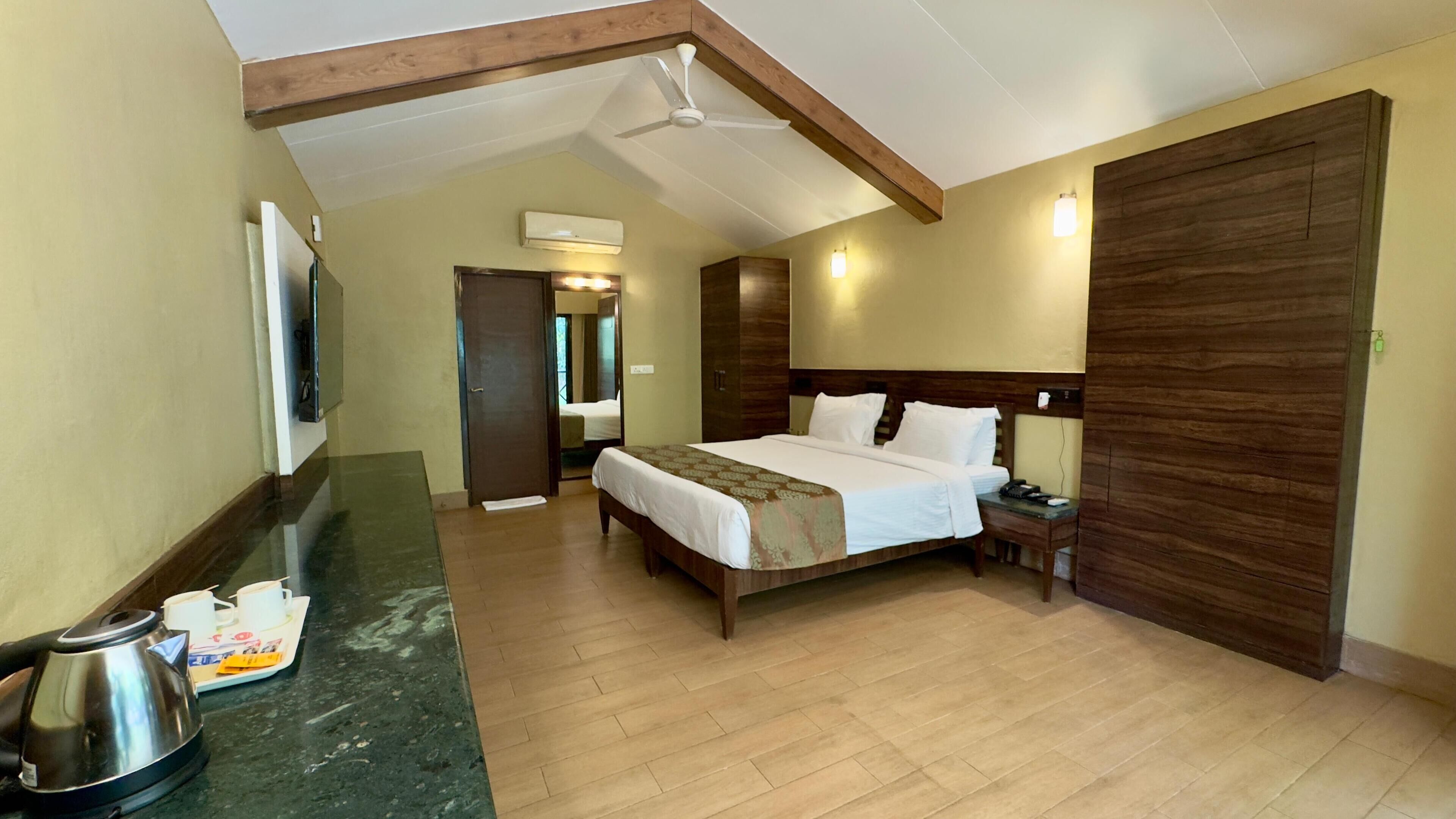 A hotel room with a bed, a nightstand, a coffee maker, a wooden wardrobe, and a ceiling fan.