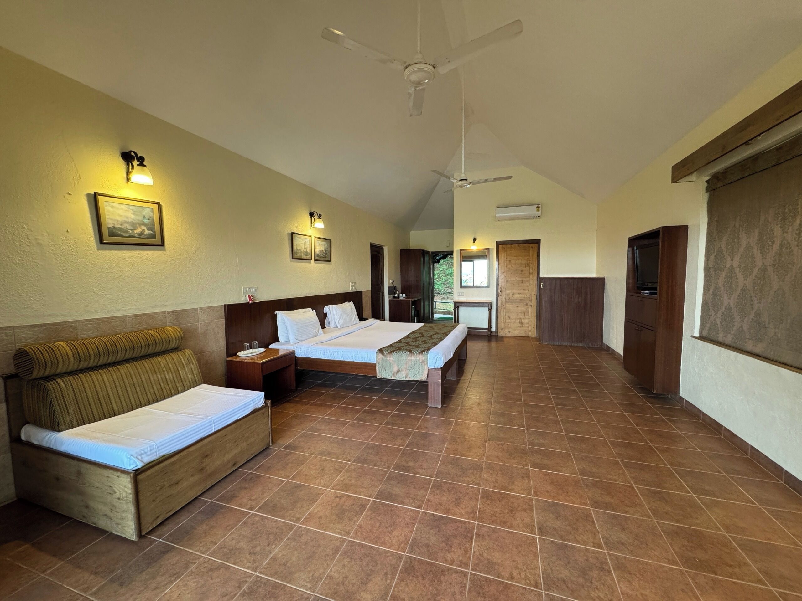 A hotel room with two beds, a bench, a TV, and a ceiling fan.