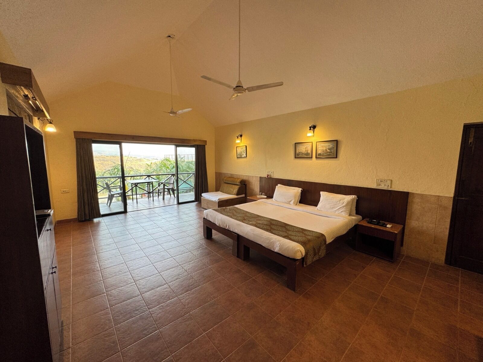 A hotel room with a large bed, a balcony with a table and chairs, and a ceiling fan.