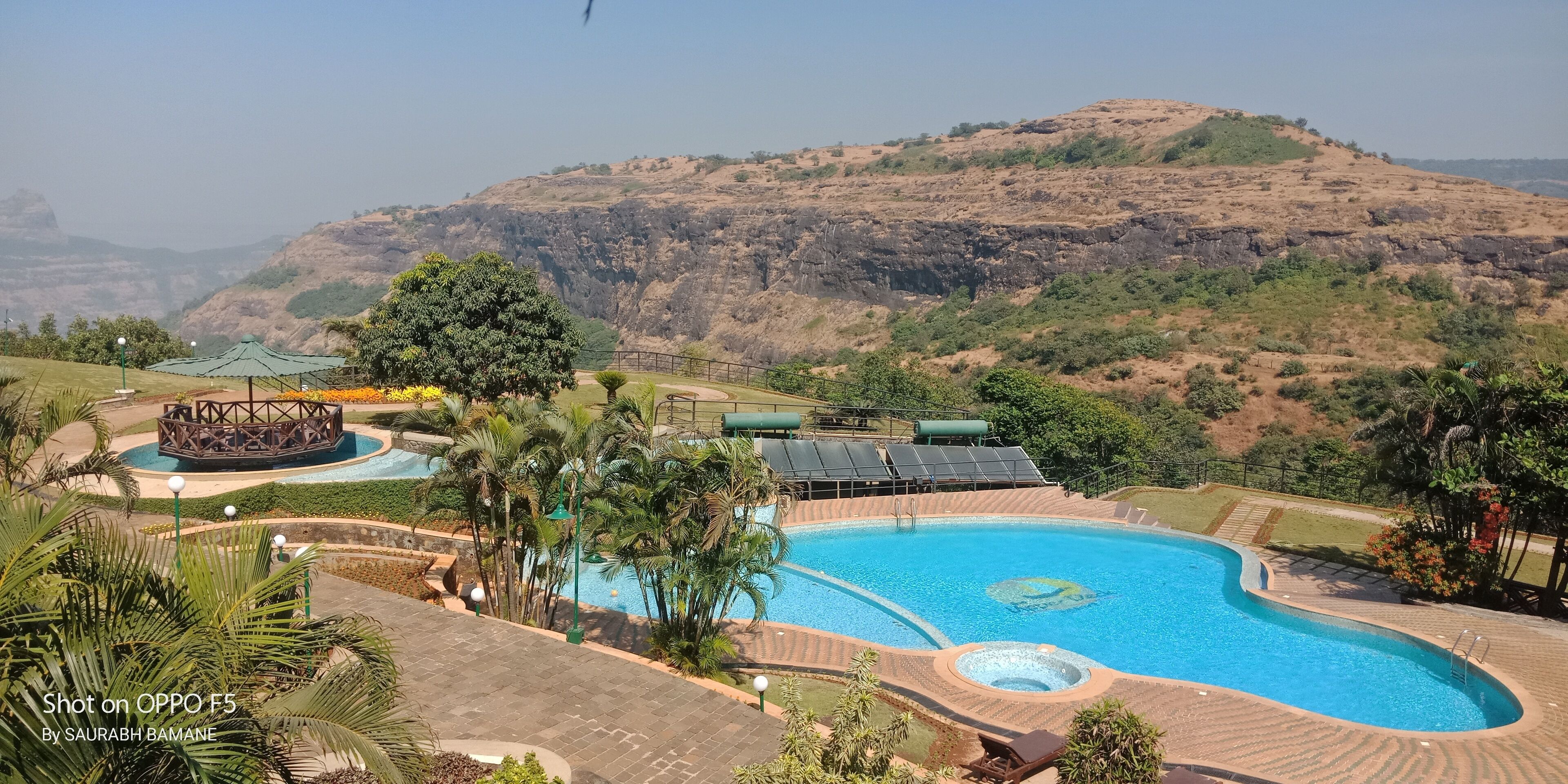 A swimming pool with a hot tub, surrounded by palm trees and a view of a hilly landscape.