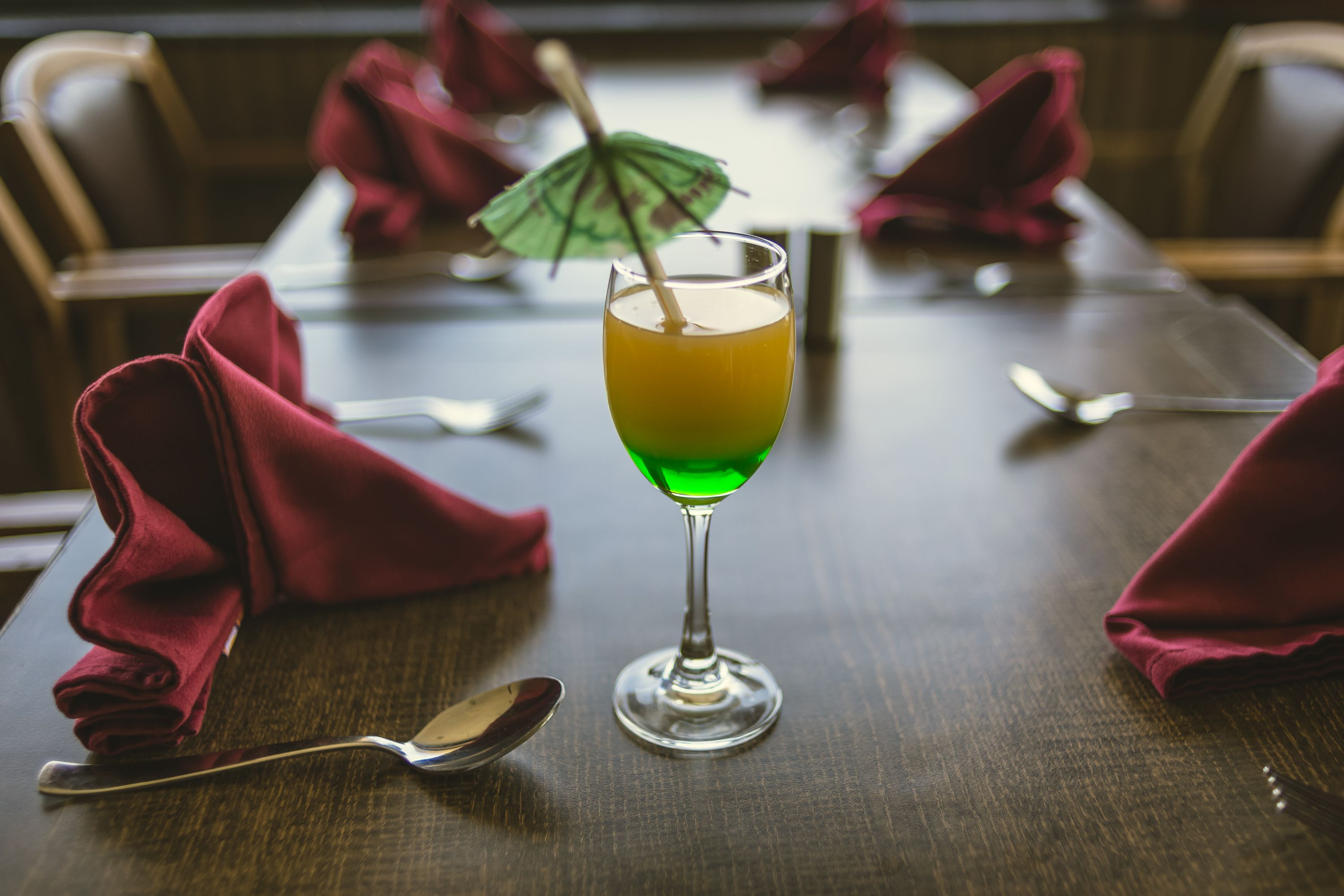 A table with a glass of orange drink, a spoon, and a folded napkin.