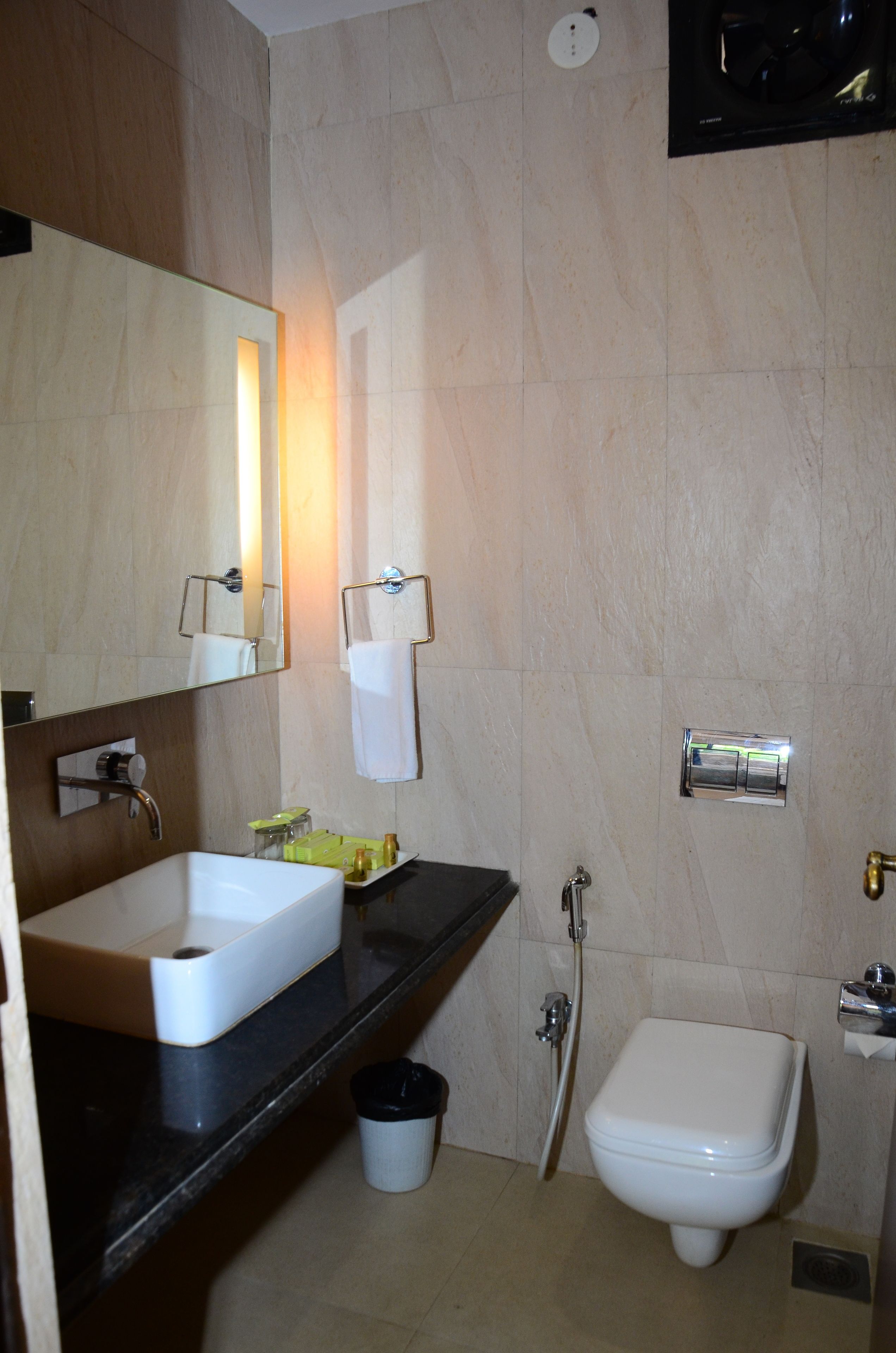 A bathroom with a sink, mirror, towel rack, toilet, and a trash bin.