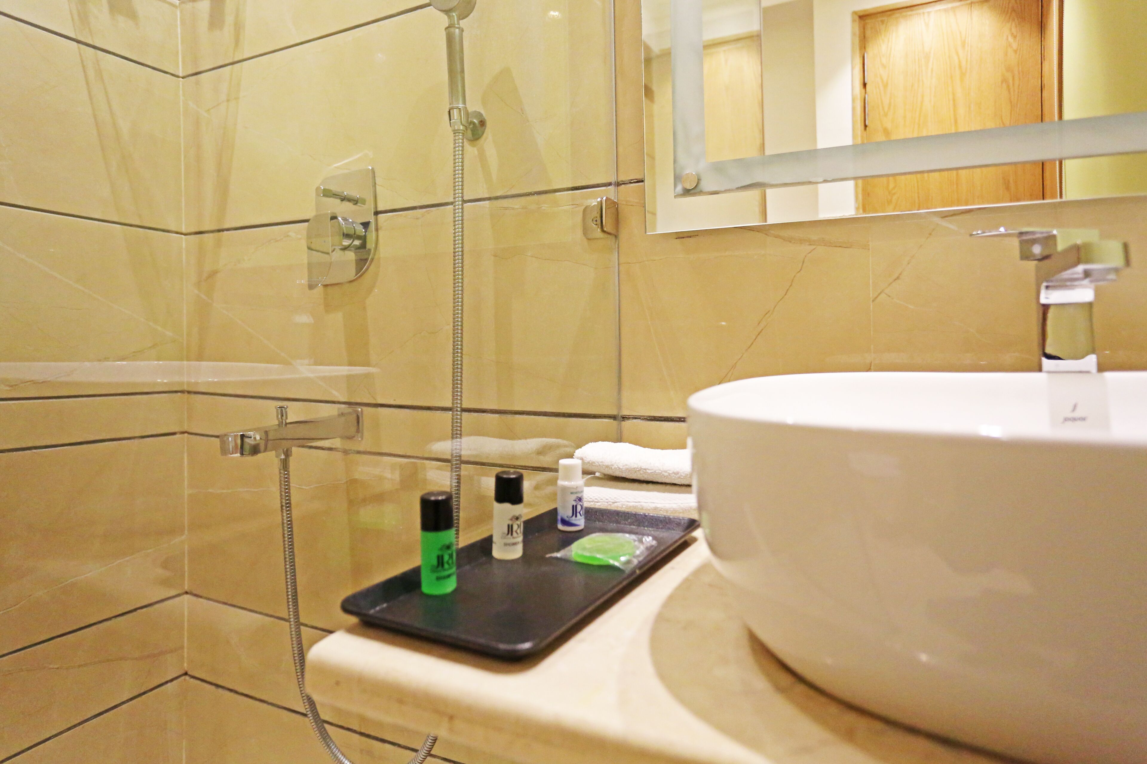 Un bagno con doccia vetrata, lavandino bianco e articoli da toilette su un vassoio.