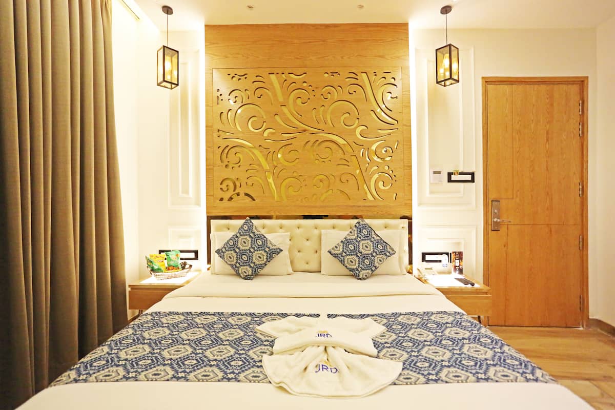 Una habitación de hotel con una cama grande, un cabecero decorativo, dos mesitas de noche con lámparas y una puerta de madera.