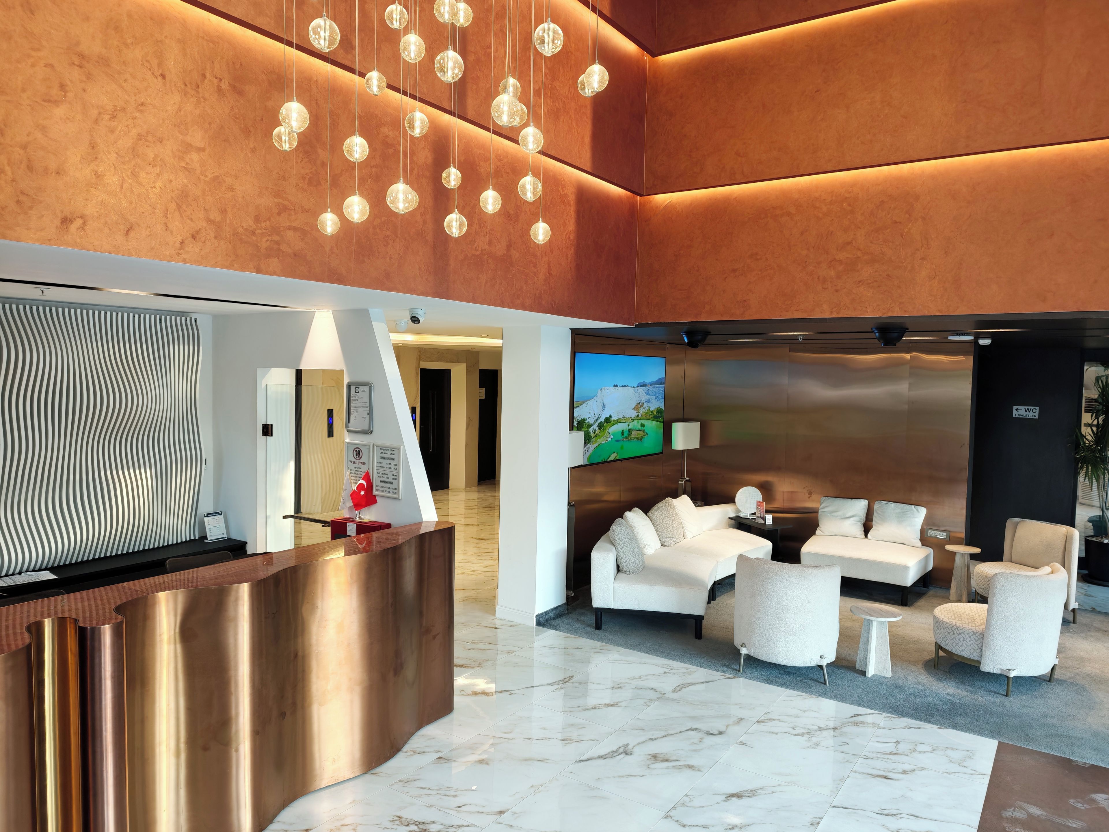 Un vestíbul modern amb taulell de recepció, zona de seients i una pantalla gran que mostra un paisatge.